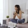 Energy Woman Sitting On Couch With Coffee And Laptop Web Size